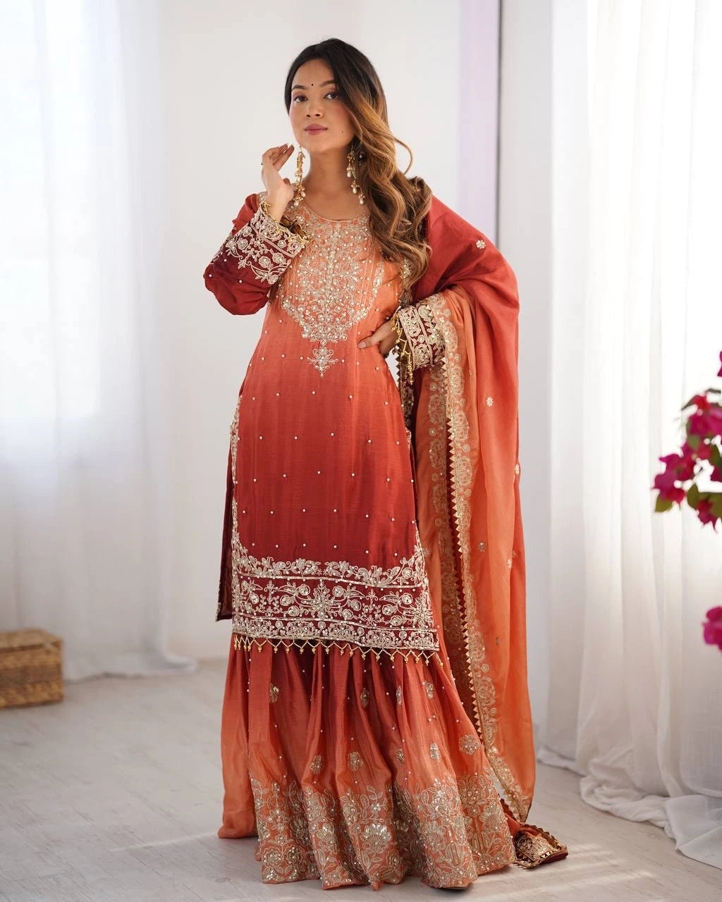 Woman wearing a traditional orange and red embroidered outfit with a white background