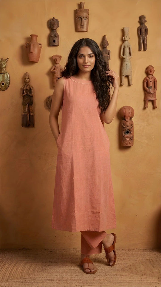 Woman in a pink dress standing against an orange wall with decorative masks.