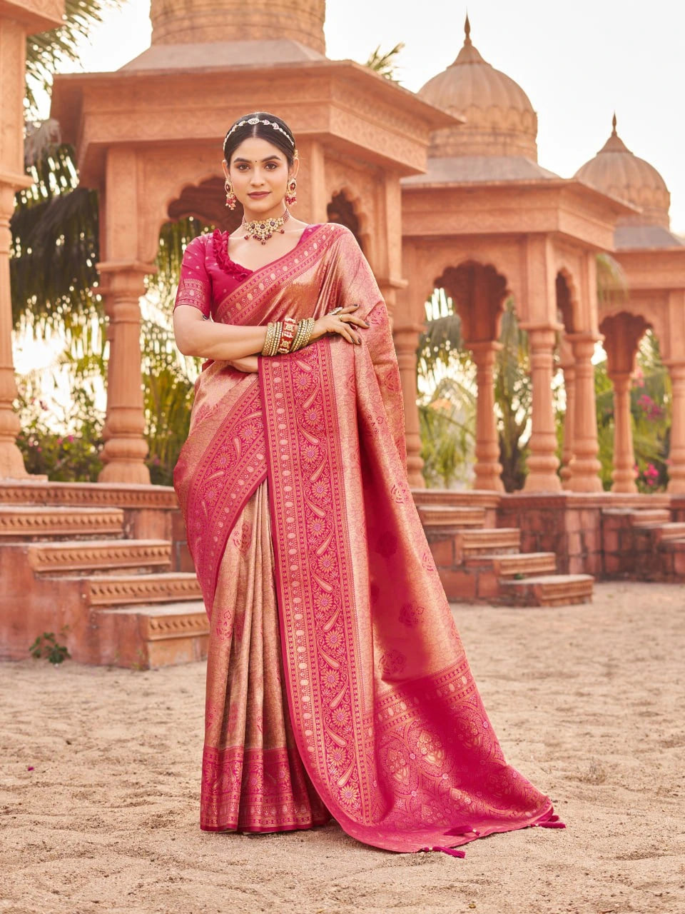 Woman in a pink saree standing in front of an architectural structure.