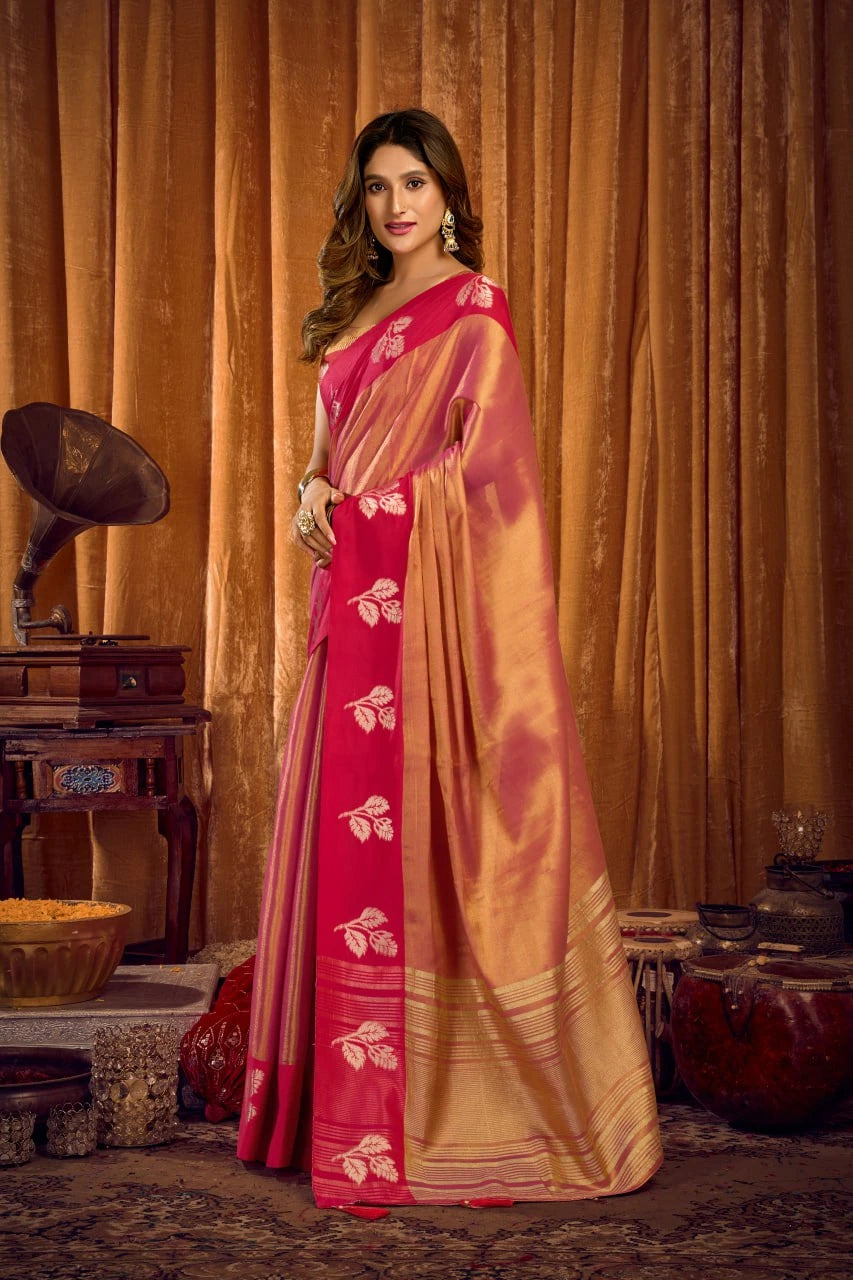 Woman in a pink and gold saree standing in front of a vintage gramophone and decorative items.