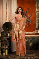 Woman in a peach saree with floral patterns standing in an elegant room.