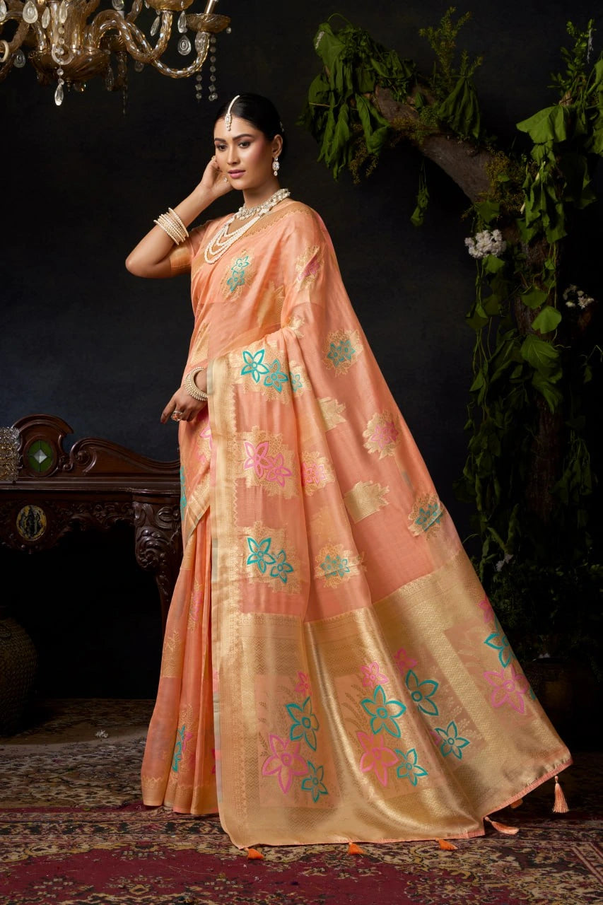 Woman in a peach saree with floral patterns standing in a decorated room.