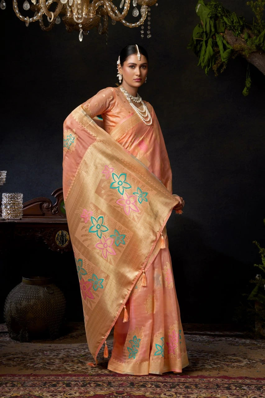 Woman in a peach saree with floral patterns in a dark room.