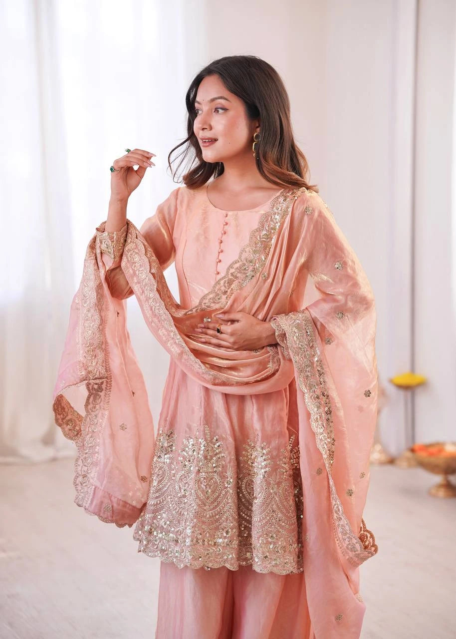 Woman wearing a peach embroidered traditional outfit in a bright room.
