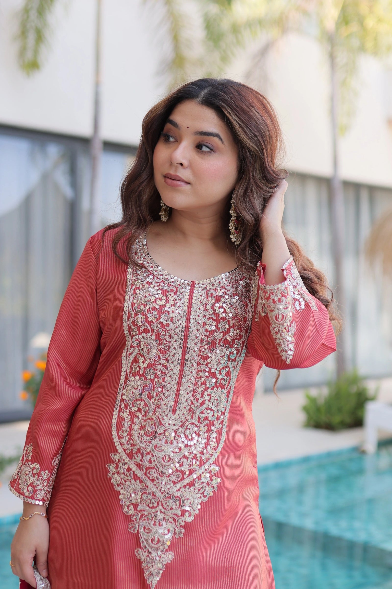 Woman wearing a pink and red embroidered traditional outfit by a poolside.