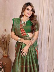 Woman wearing a green saree with a matching blouse, standing against a beige curtain.