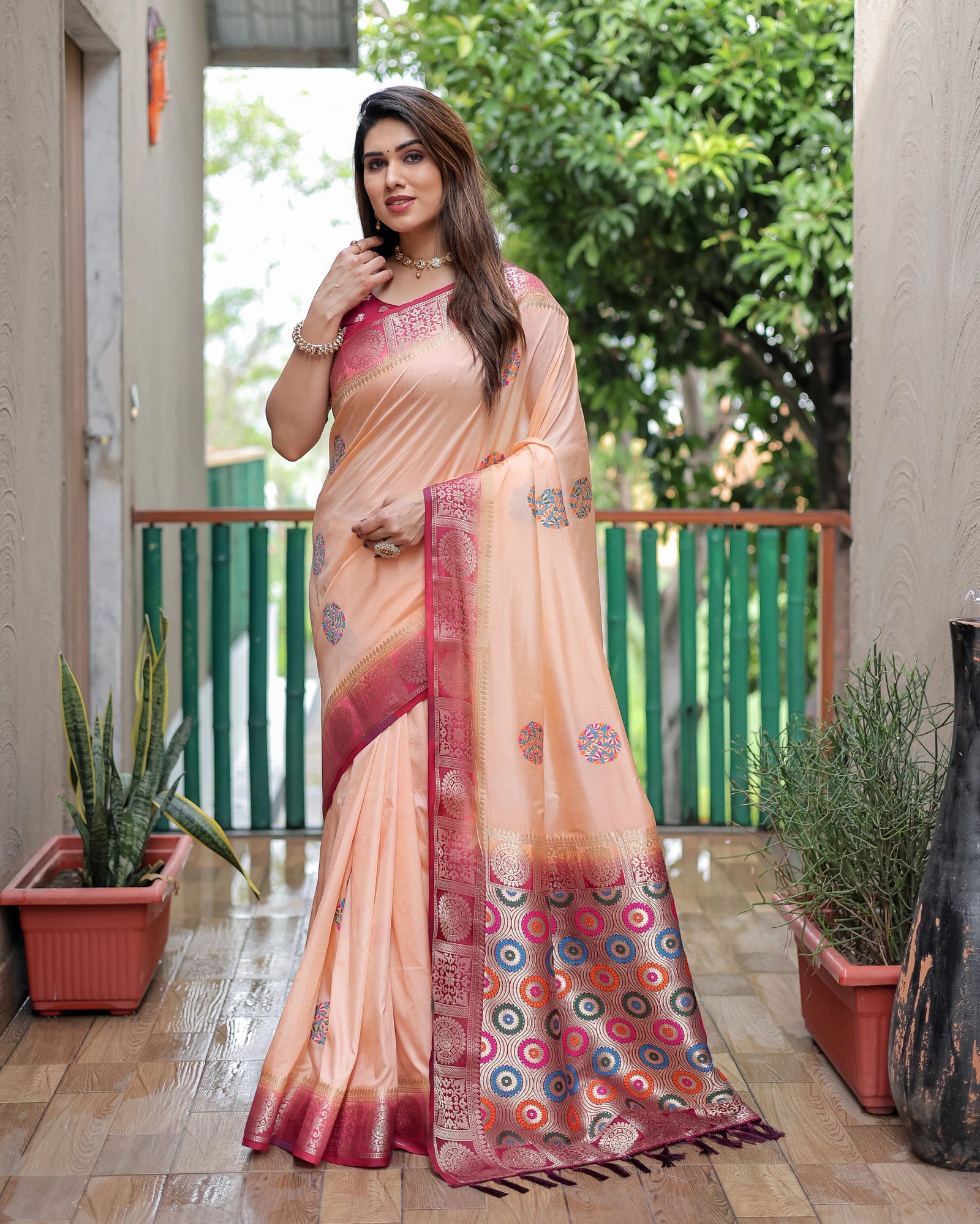Woman wearing a peach saree with a colorful border on a wooden floor.