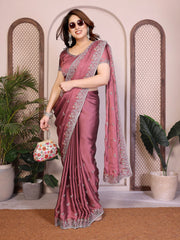 Woman in a pink saree with a floral bag standing in front of decorative plants.