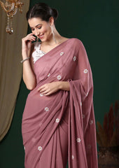 Woman wearing a mauve saree with white floral patterns against a green background