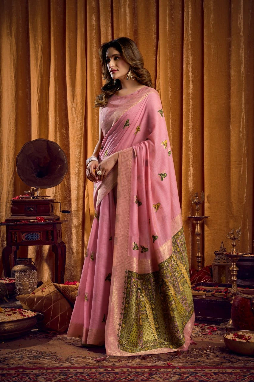 Woman in a pink saree with green border standing in an elegant room.