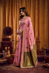 Woman in a pink saree with green border standing in an elegant room.