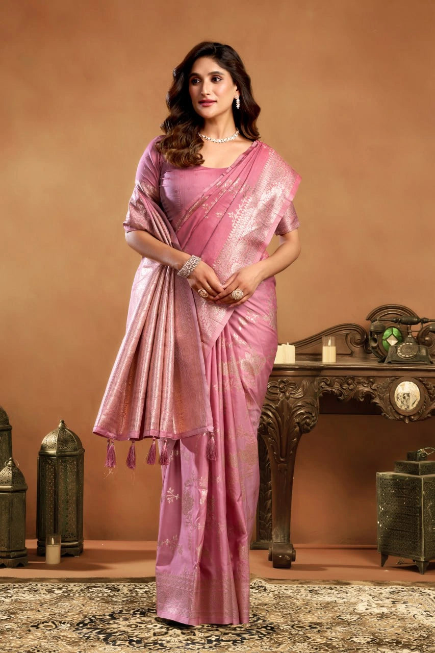 Woman in a pink saree standing in front of a decorative background