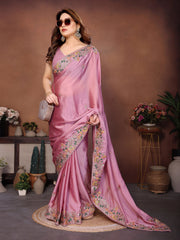 Woman in a pink saree with floral patterns standing in a decorated room.