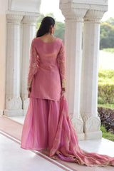 Woman in a pink traditional outfit standing in front of white marble pillars with a garden view.
