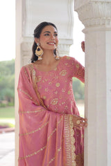 Woman in a pink saree with gold embroidery standing in front of a white architectural structure.