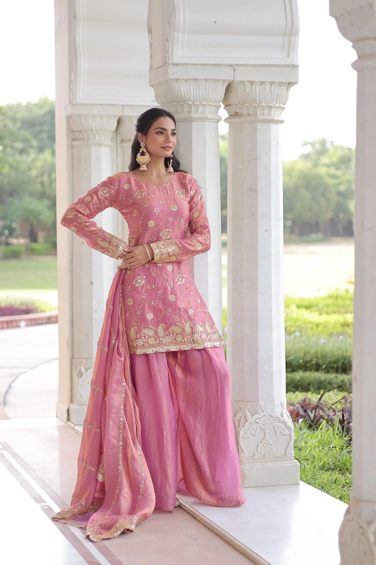 Woman in a pink traditional outfit standing in a garden setting.