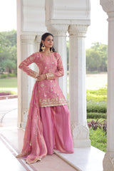 Woman in a pink traditional outfit standing in a garden setting.