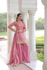 Woman in a pink traditional outfit standing in a garden setting.