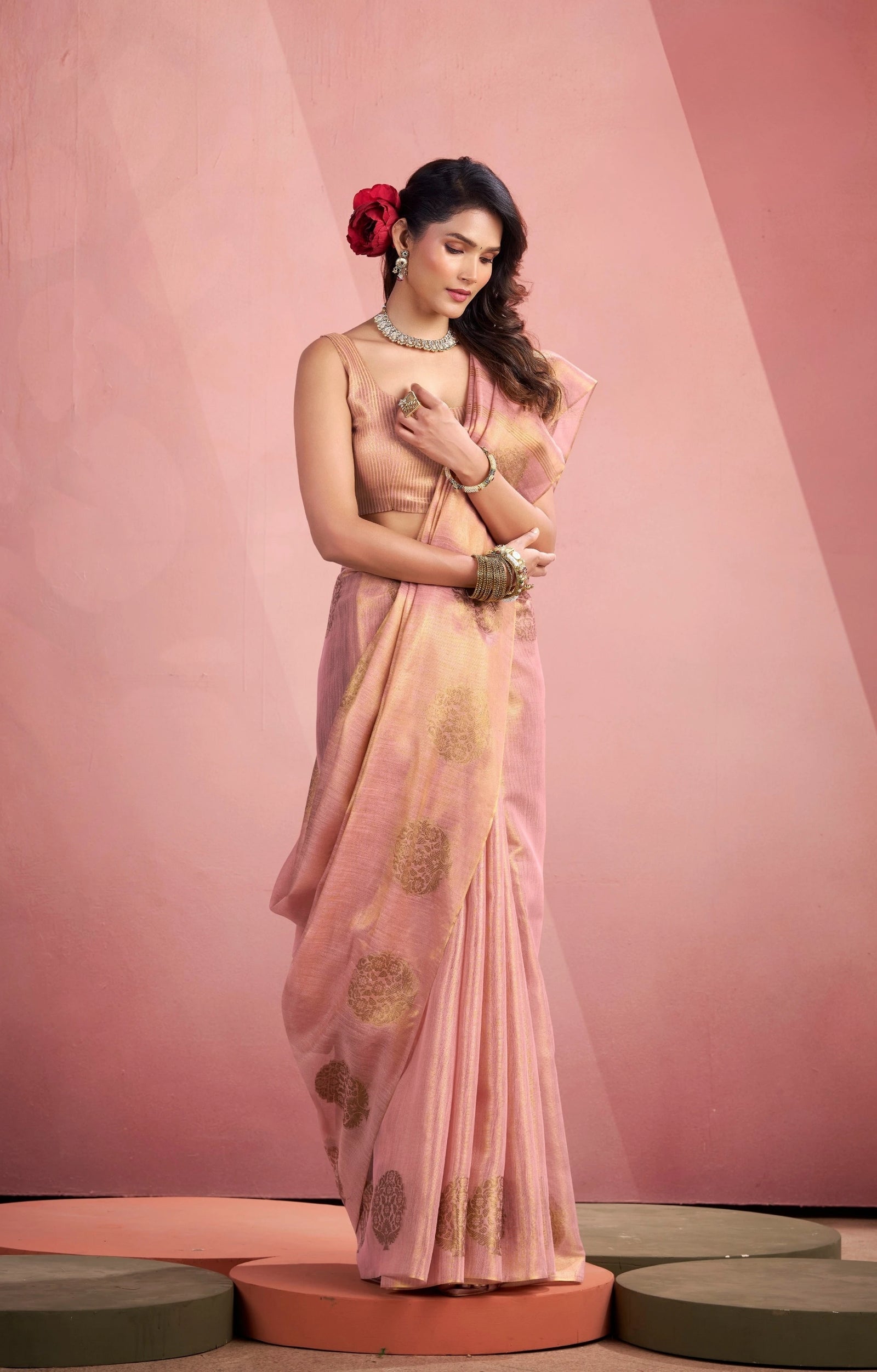 Woman in a light pink saree with gold patterns on a pink background