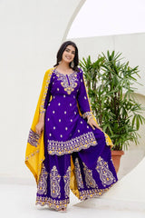 Woman in a purple and yellow traditional outfit sitting outdoors with plants in the background