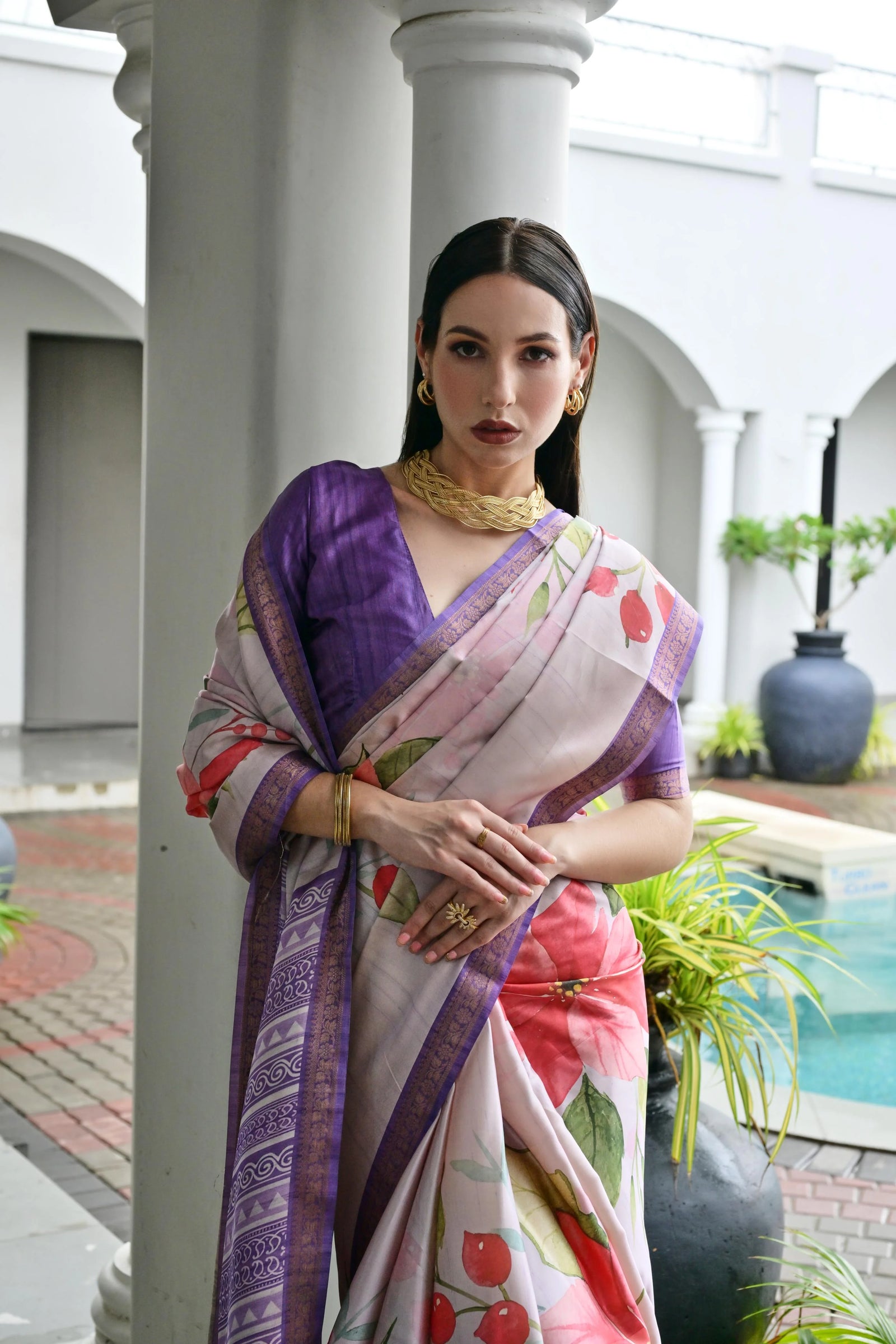 Woman wearing a colorful saree in an outdoor setting with columns and plants.