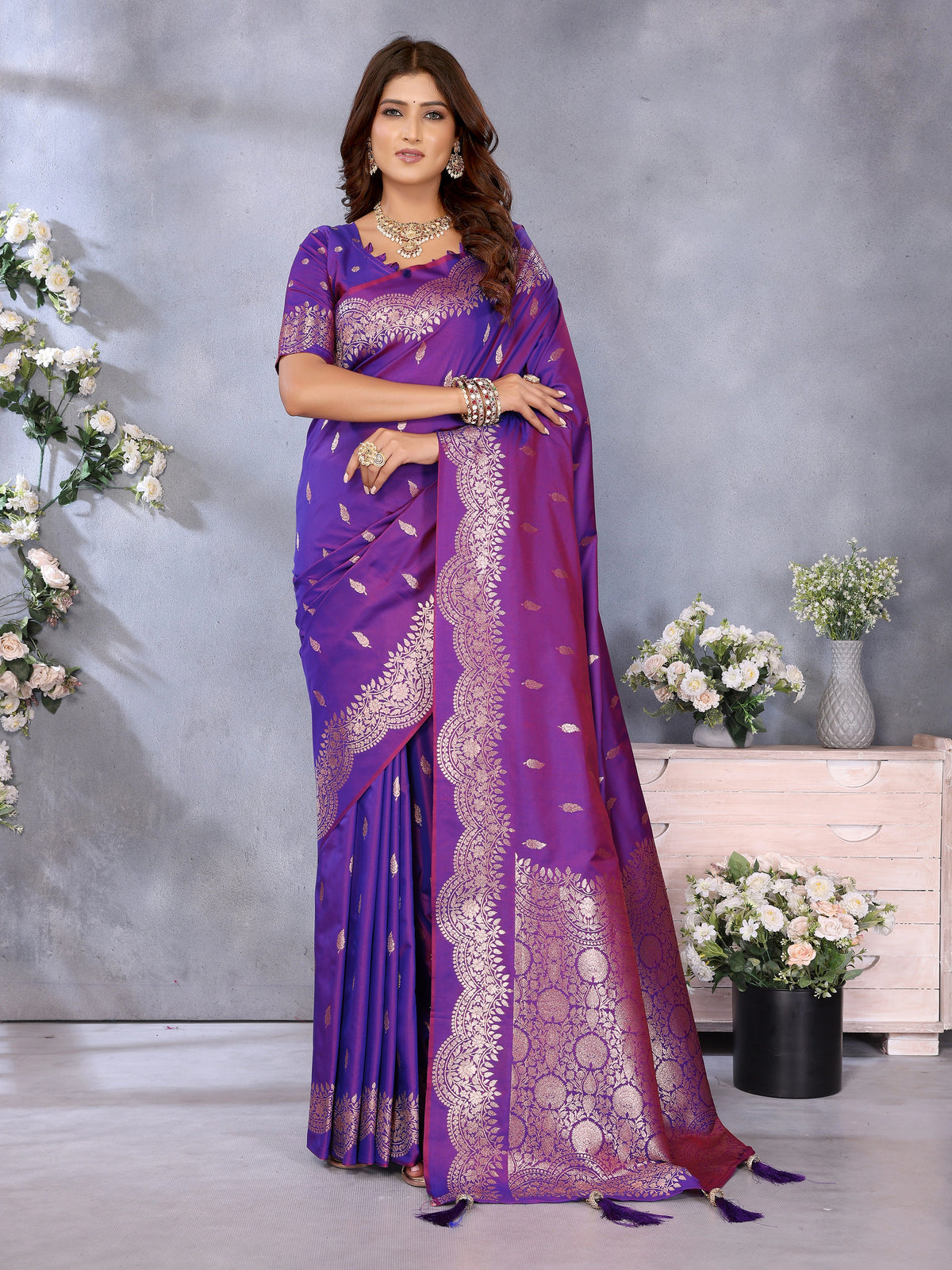 Woman wearing a purple saree with white patterns in a decorated room.