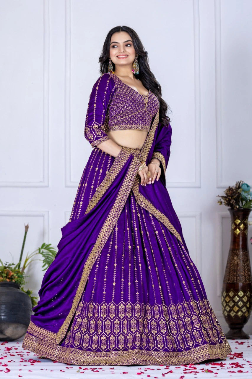 Woman wearing a purple saree with gold border against a white wall.