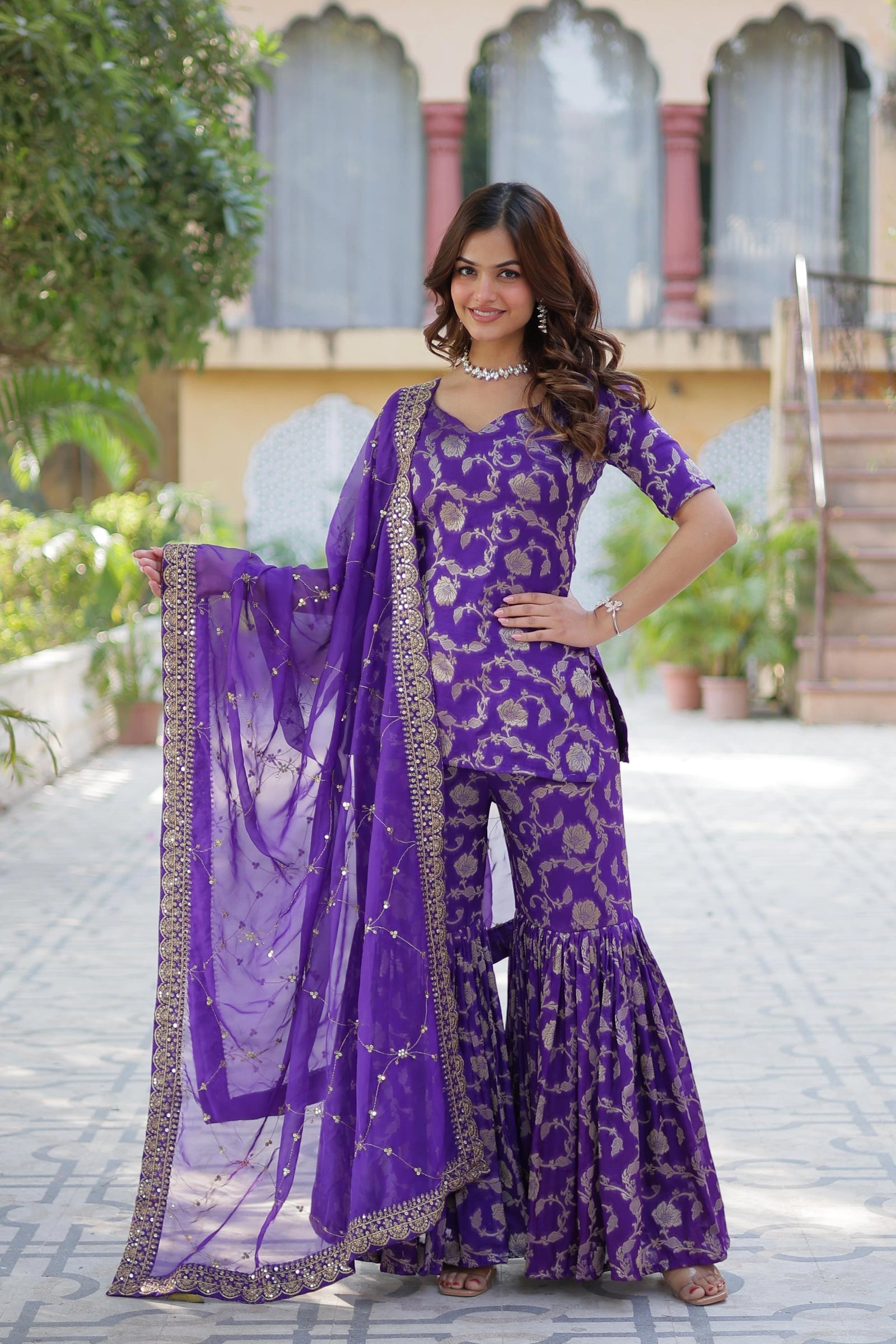 Woman in a purple traditional outfit with a matching dupatta standing outdoors.