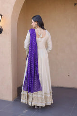 Woman wearing a white dress with a purple dupatta in an outdoor setting.