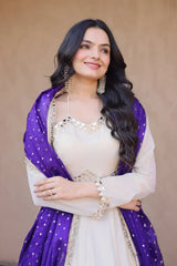 Woman wearing a white outfit with a purple dupatta against a beige background