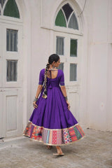 Woman in a purple dress with a colorful skirt standing in front of a white building.