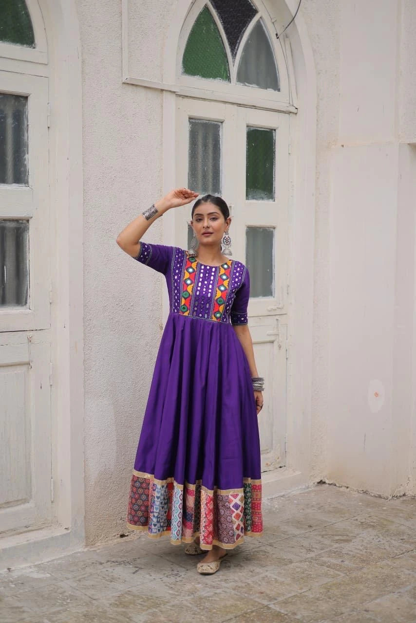 Woman wearing a purple dress with colorful patterns in front of a white wall.