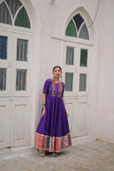 Woman in a colorful dress standing in a room with white walls and large windows.