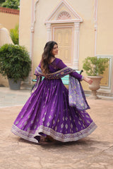 Woman in a purple traditional outfit standing outdoors with decorative elements in the background