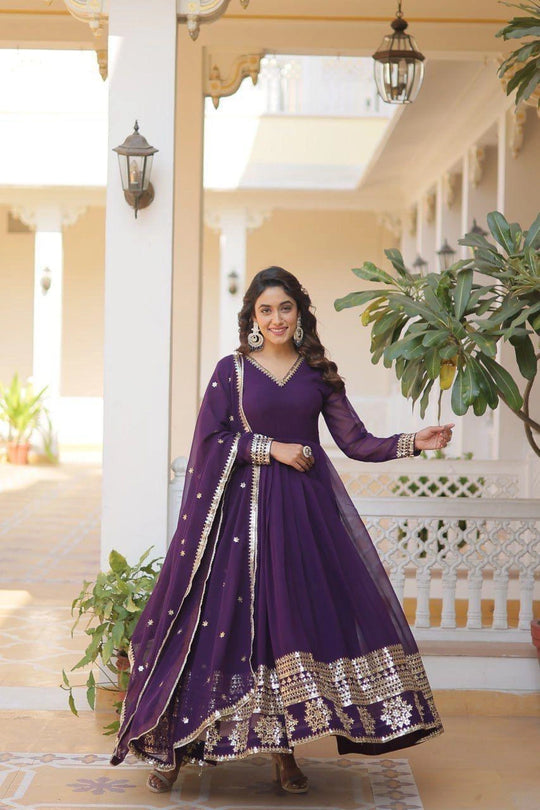 Woman in a purple traditional outfit standing in a well-lit room with plants.