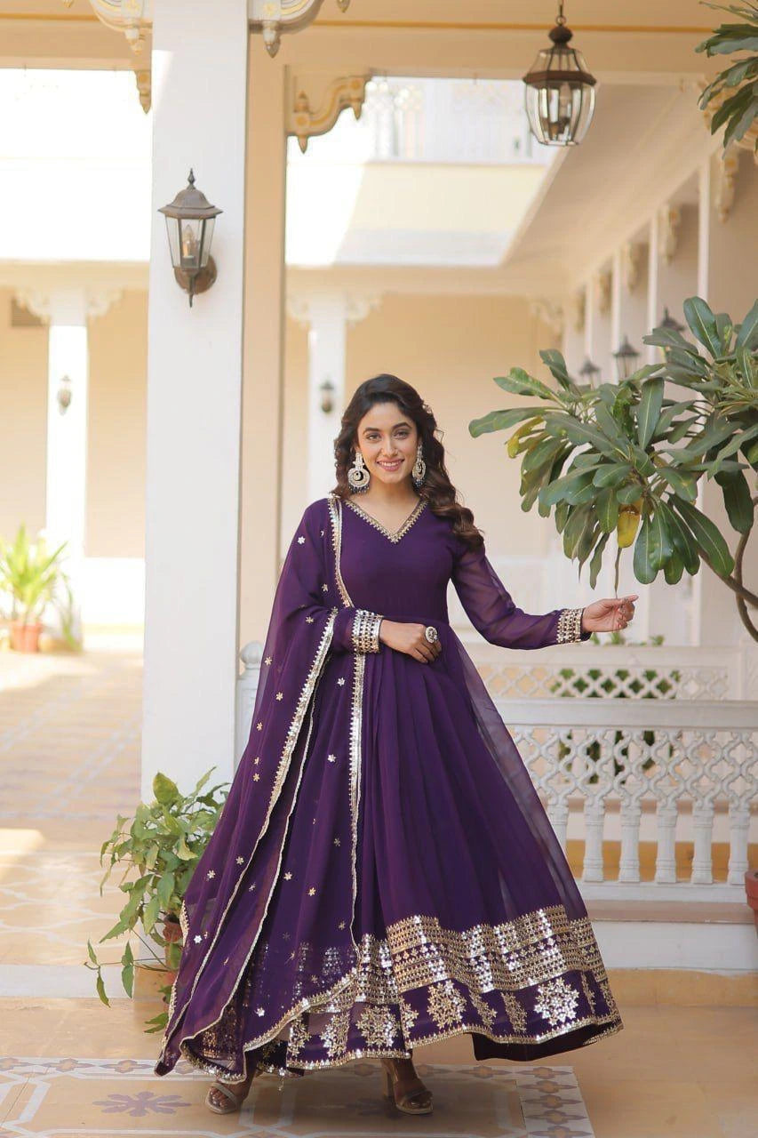 Woman in a purple traditional outfit standing in a well-lit room with plants.