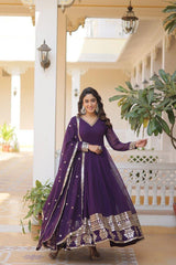 Woman in a purple traditional outfit standing in a well-lit room with plants.