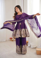 Woman in a purple traditional outfit with gold embroidery in a bright room.