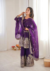 Woman in a purple traditional outfit with white embroidery standing in a bright room.