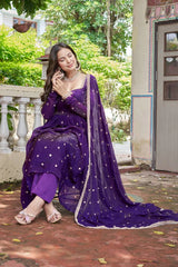 Woman in a purple traditional outfit sitting outdoors with greenery in the background