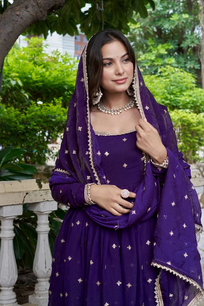 Woman in a purple traditional outfit with a matching dupatta, standing outdoors.