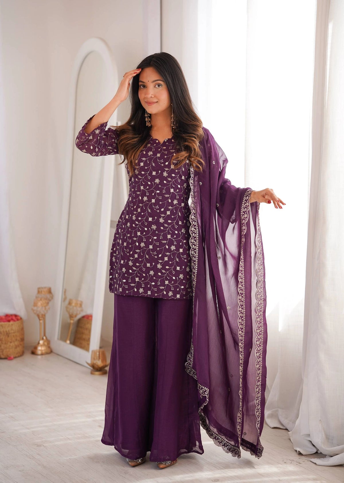 Woman in a purple traditional outfit with a matching dupatta in a bright room.