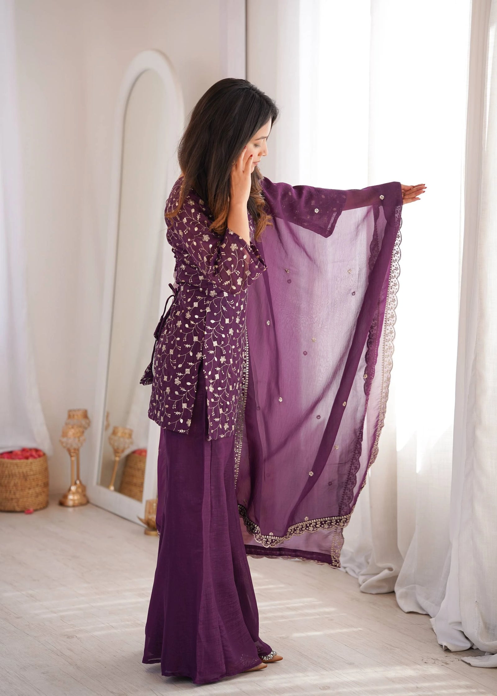Woman in a purple outfit with a matching scarf in a room with white curtains.