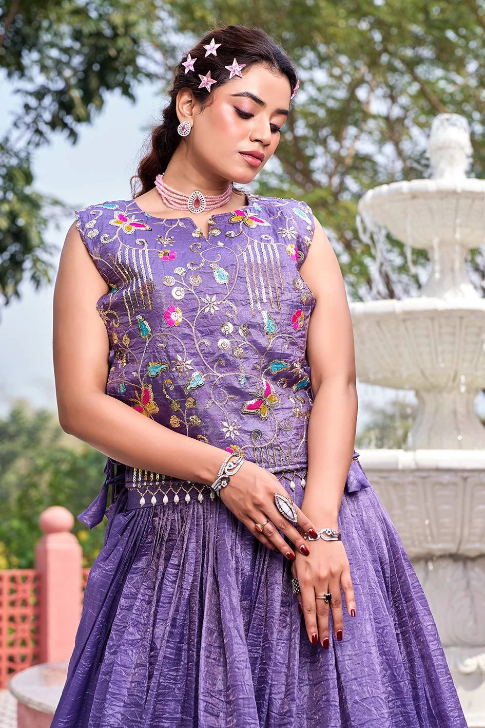 Woman wearing a purple embroidered outfit with a fountain in the background