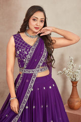 Woman wearing a purple saree with silver details against a beige background