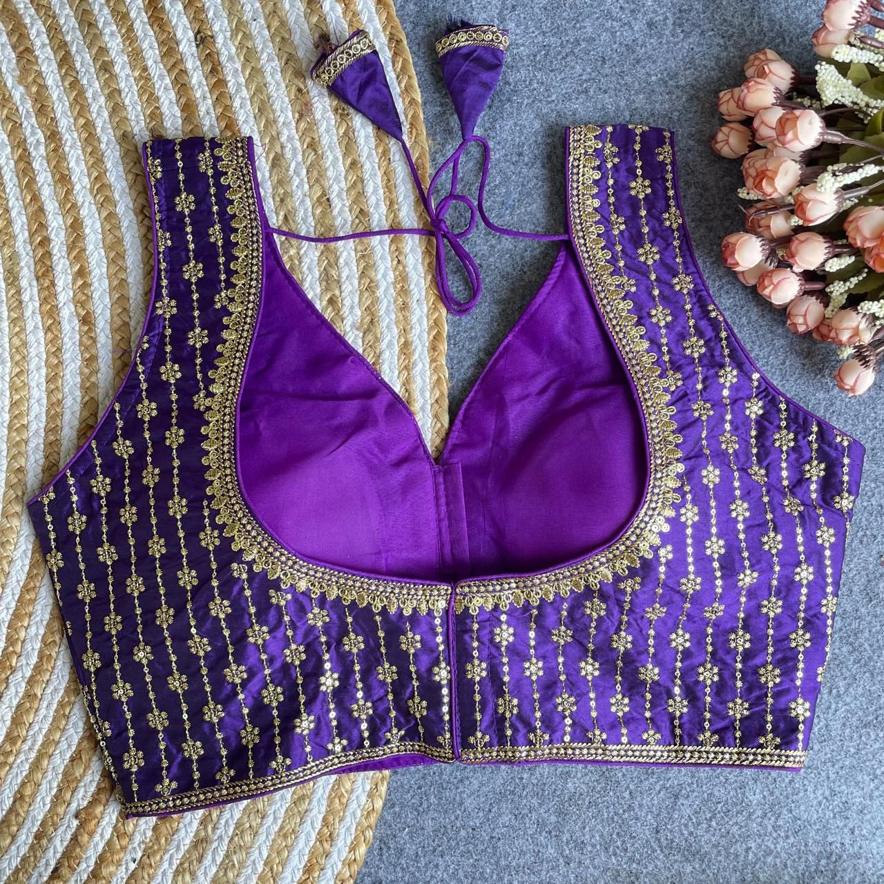 Purple embroidered blouse with gold details on a textured surface with flowers.