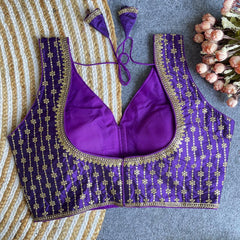 Purple embroidered blouse with gold details on a textured surface with flowers.