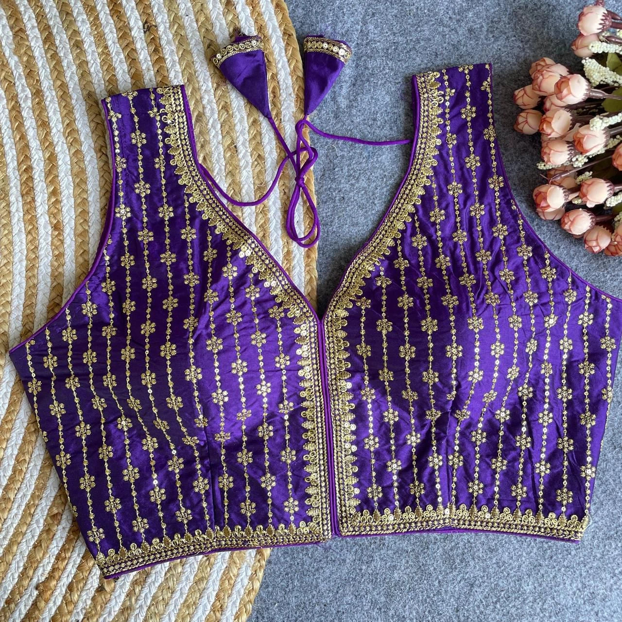 Purple embroidered top with gold details on a textured surface with flowers.