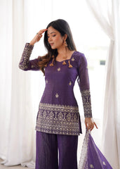 Woman wearing a purple traditional outfit with intricate designs against a white curtain background