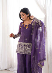 Woman wearing a traditional purple outfit with intricate designs against a white curtain background